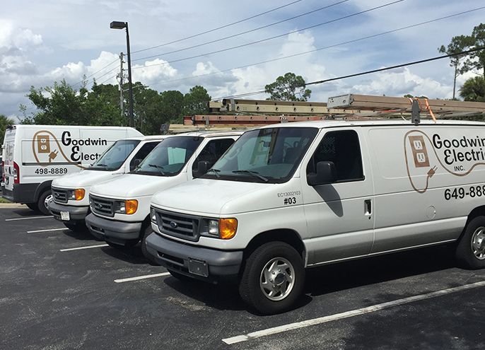 A row of goodwin electric vans are parked in a parking lot.