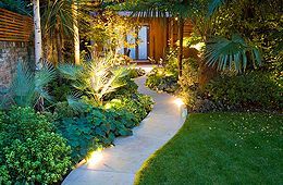 A path leading to a house in a lush green garden at night.