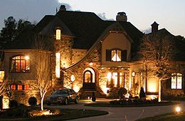 A large house is lit up at night with a car parked in front of it.