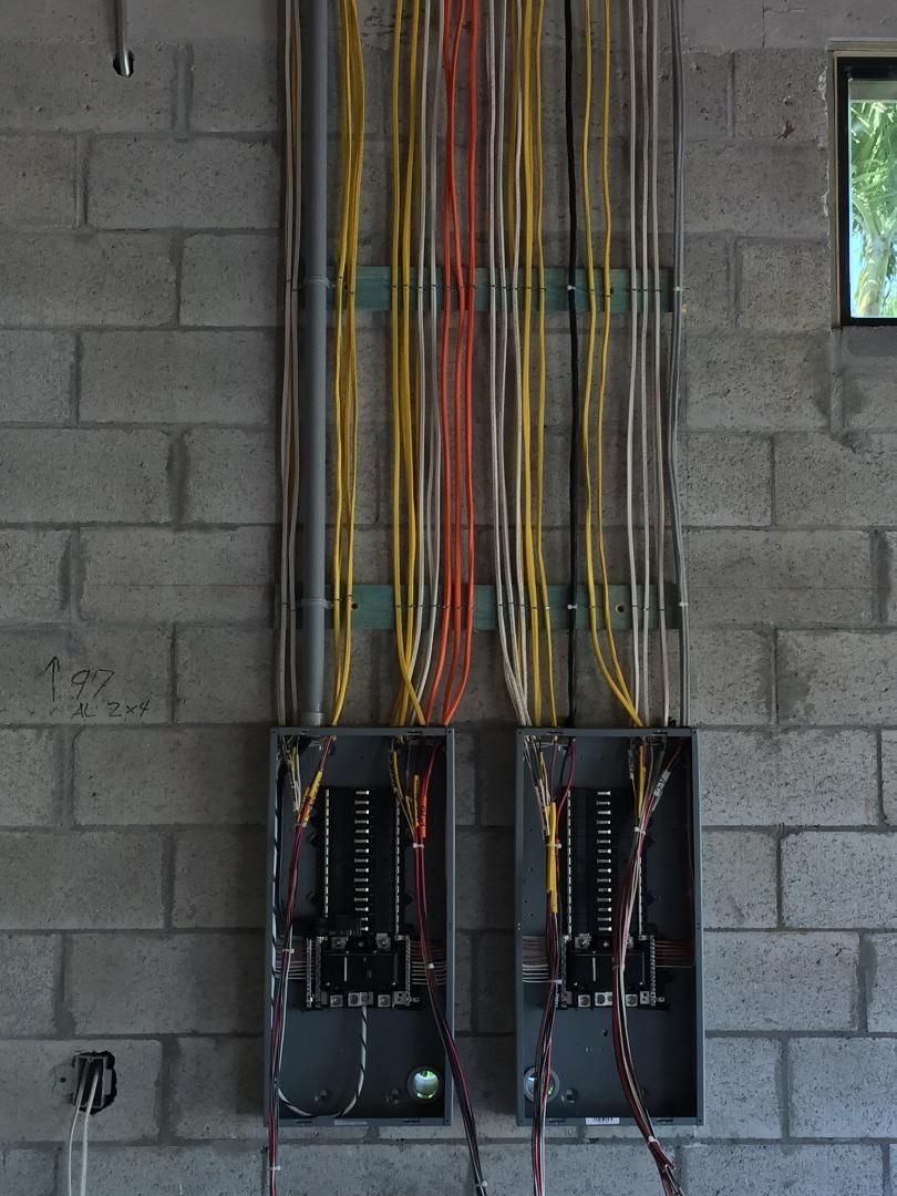 Two electrical boxes are hanging on a brick wall.