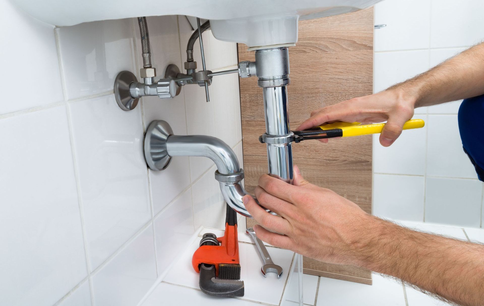 A plumber is fixing a sink pipe with a wrench.