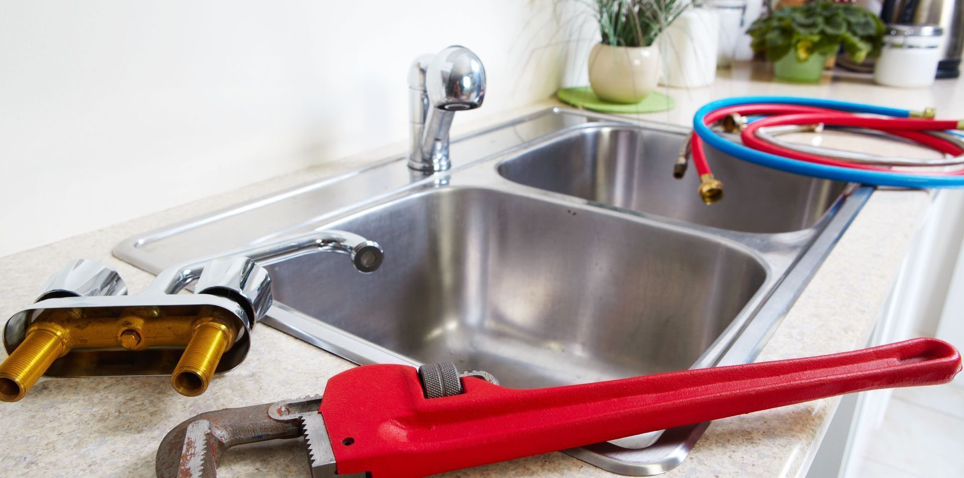 A kitchen sink with a wrench and hose on the counter.