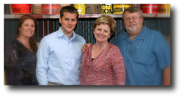 Four people posing together indoors, smiling in front of shelves and red containers.