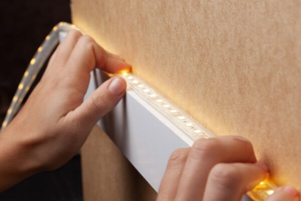 Hands installing a white LED strip along the edge of a wall panel