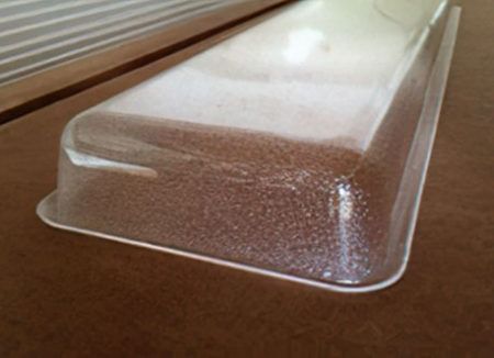 Clear plastic food tray on a wooden surface with a raised lid and textured bottom