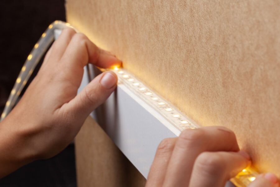 Hands installing a glowing LED strip along a wall edge