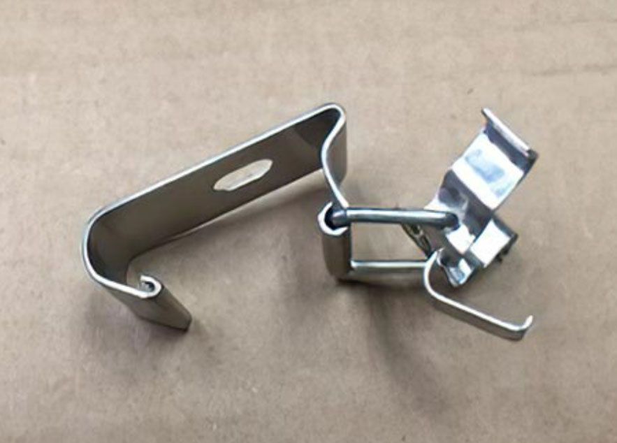 Metal spring clamp with silver jaws and black wire handle on a brown background