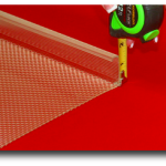 Close-up of a green-and-black tape measure marking a red surface with a pencil.