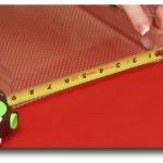 Yellow measuring tape on red textured fabric held by a hand.