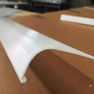 White ribbed plastic trim piece on a wooden surface, shown in close-up