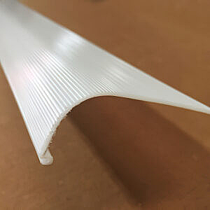 White ribbed plastic corner trim piece on a brown surface