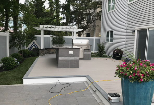 A patio with a grill and a pot of flowers in front of a house.