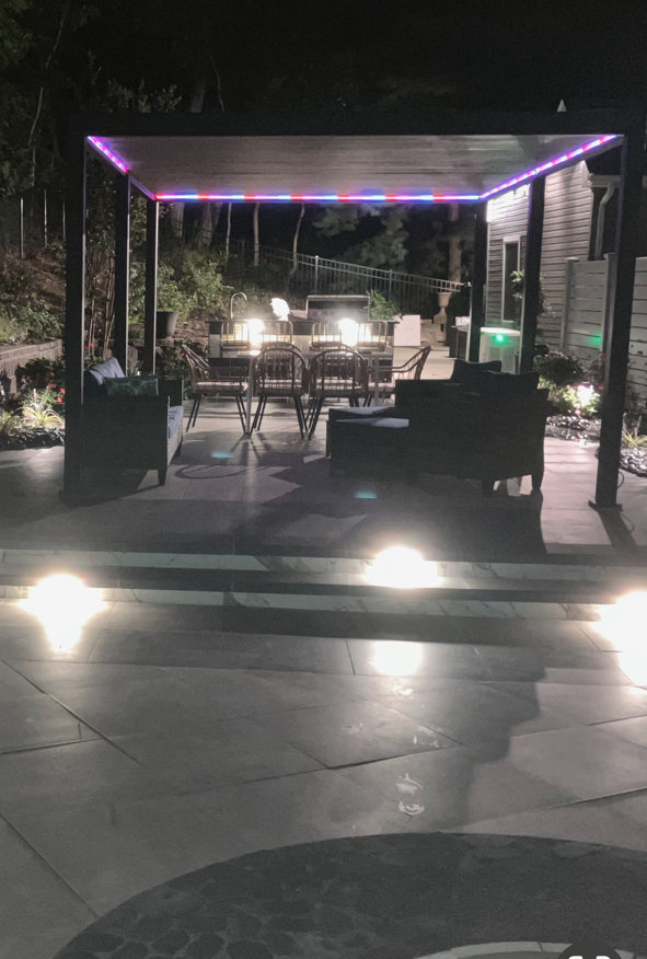 A patio with a pergola and a table and chairs at night.