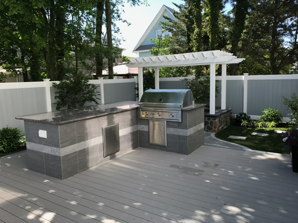 A patio with a grill and a pergola in the backyard