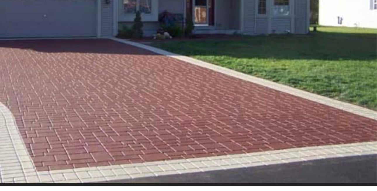 A red brick driveway with a white border is in front of a house.
