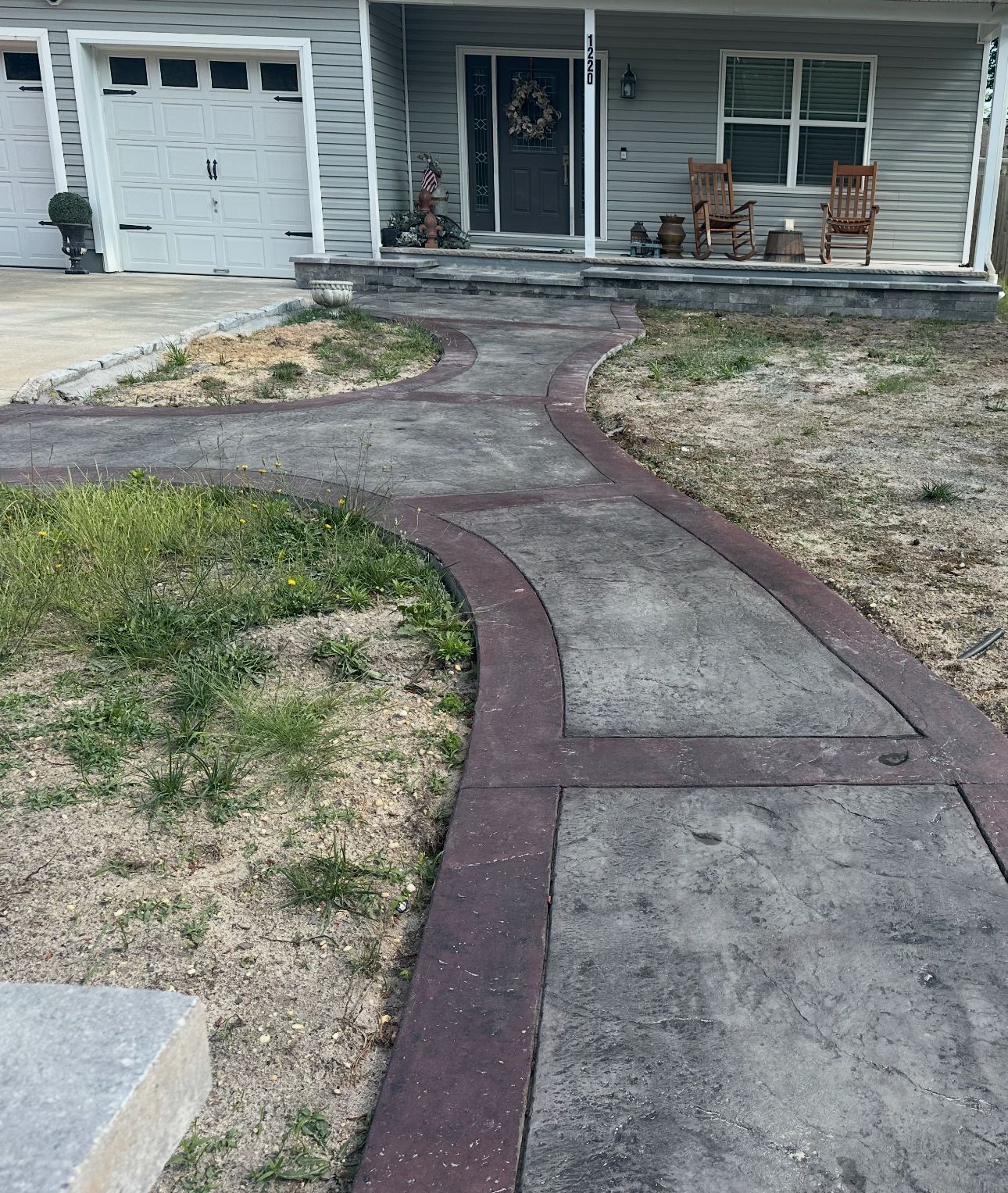 A concrete walkway leading to a house with chairs on the porch.