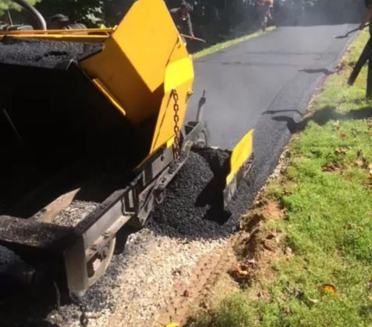 A yellow and black machine is laying asphalt on a road.