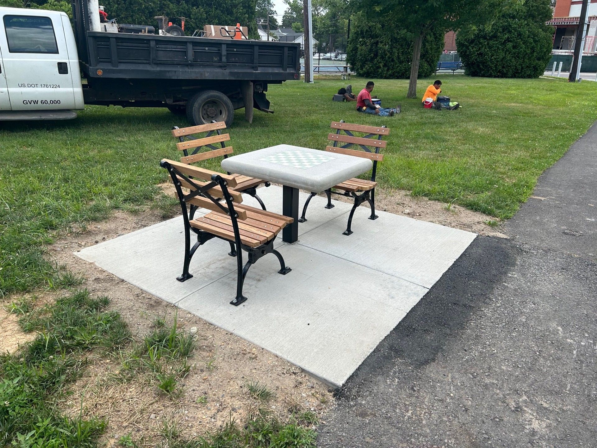 A table and benches in a park with a dump truck in the background.