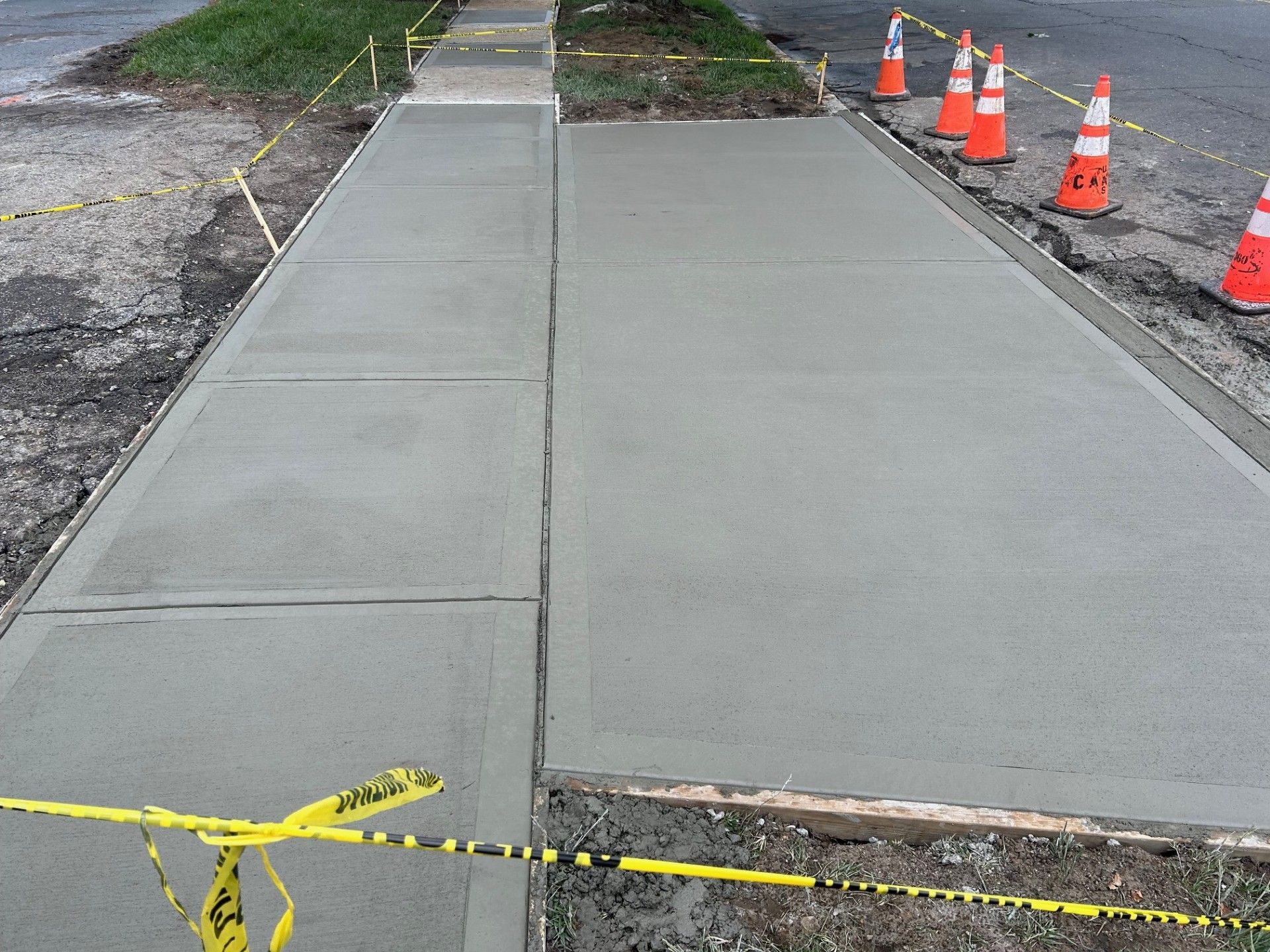 A sidewalk is being built with orange cones and yellow tape.