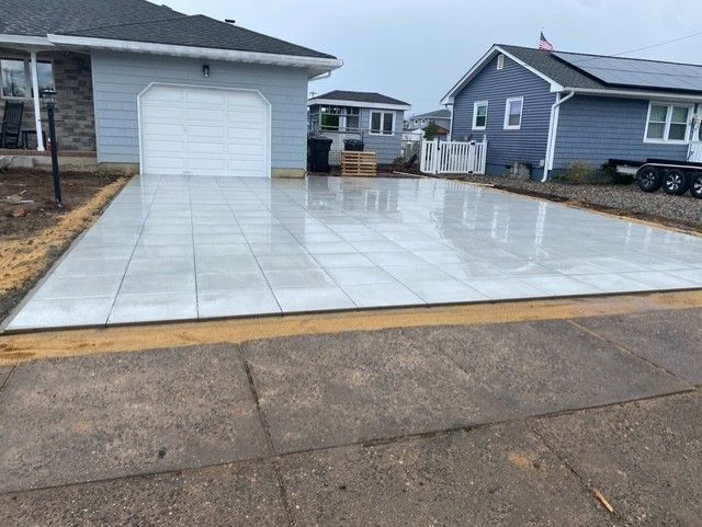 Freshly paved driveway beside a white garage, with wet concrete and neighboring houses in the background.
