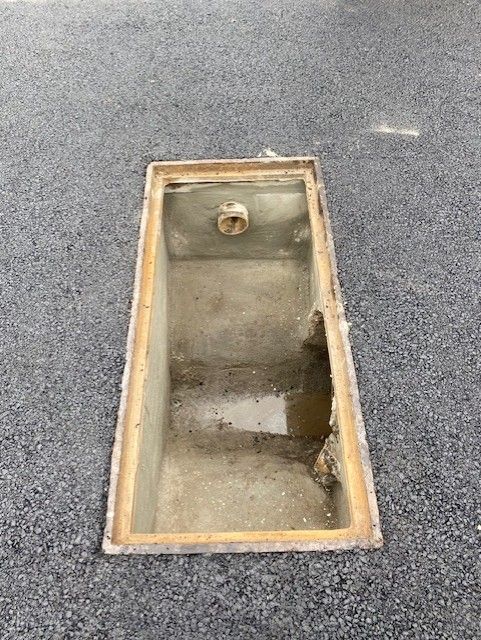 Rectangular recessed floor drain with standing water in a gray carpeted floor.