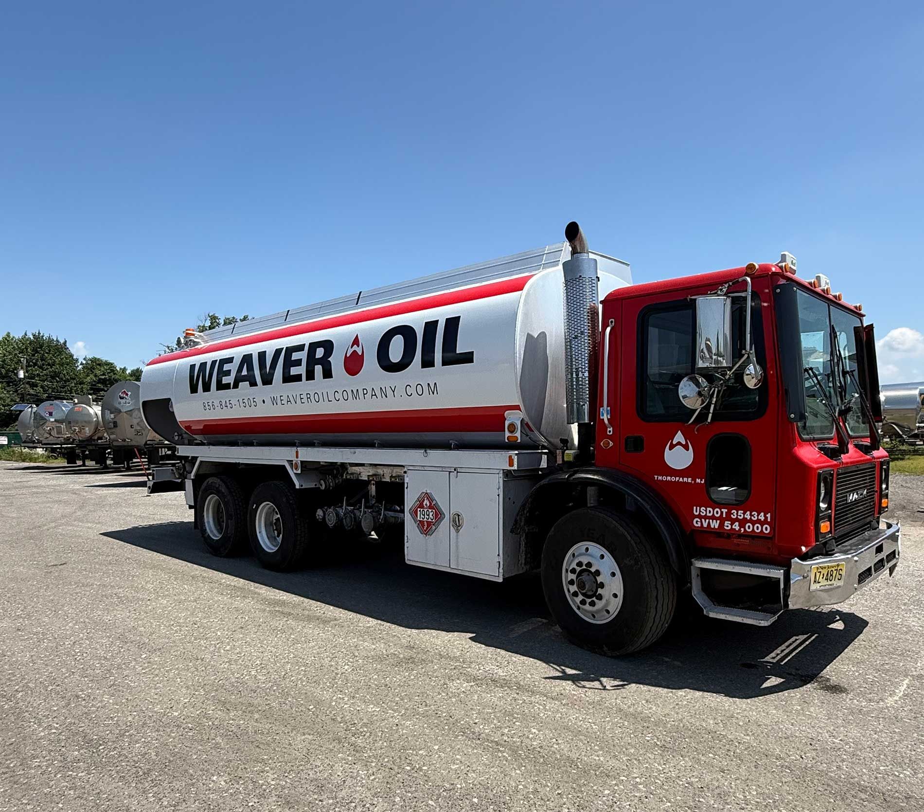 Red and white Weaver Oil tanker truck parked on gravel. Clear sky.