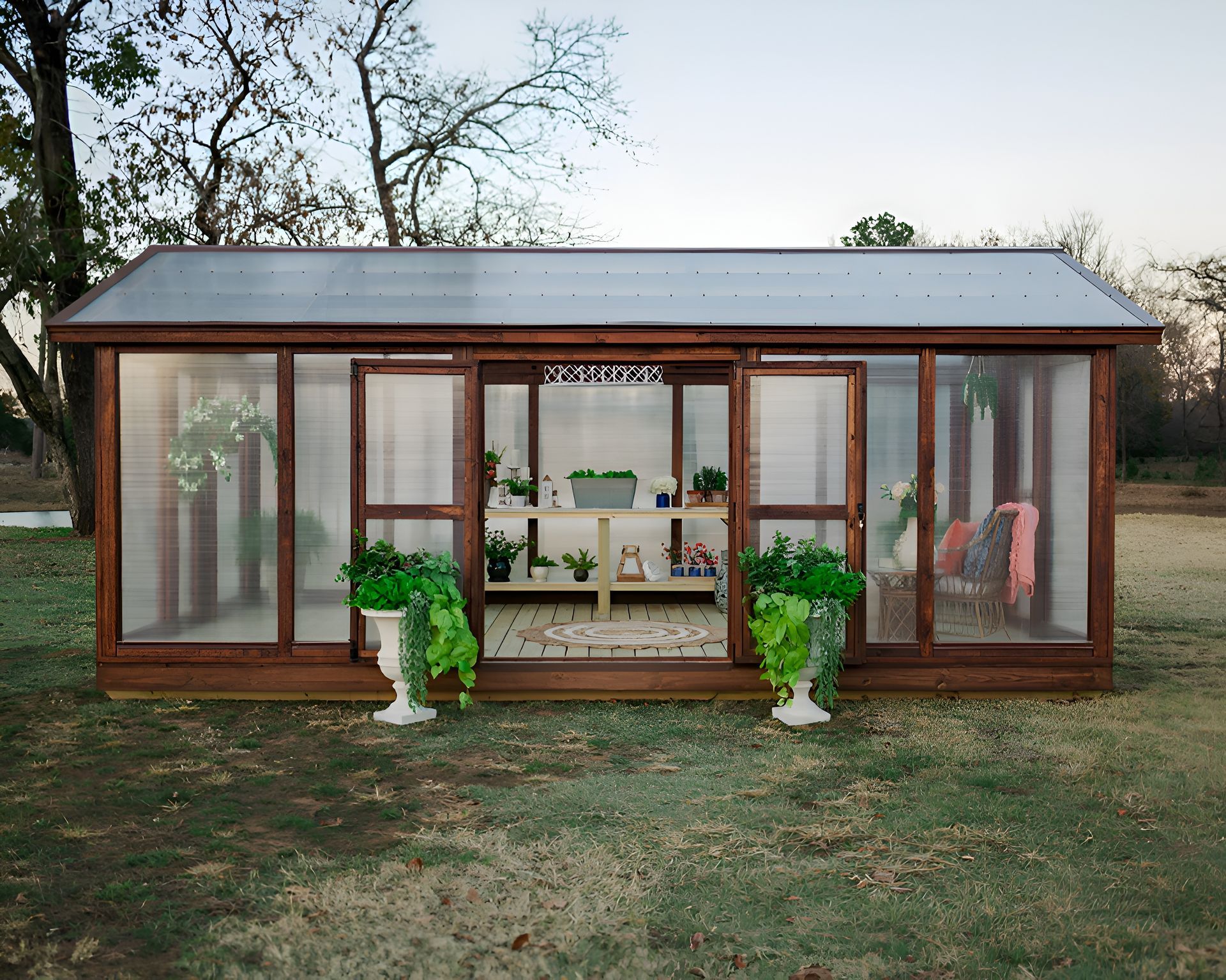 Wooden greenhouse with open doors, plants, and interior shelving on a grassy lawn.
