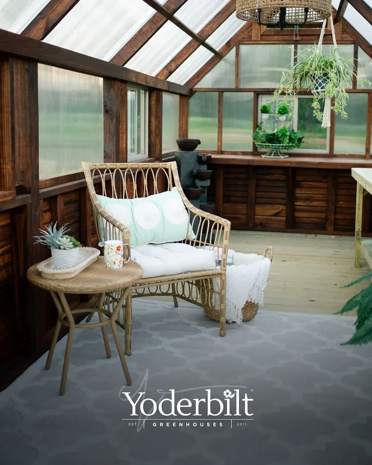 Cozy greenhouse interior with wicker chair, small table, and plants on a gray patterned rug.