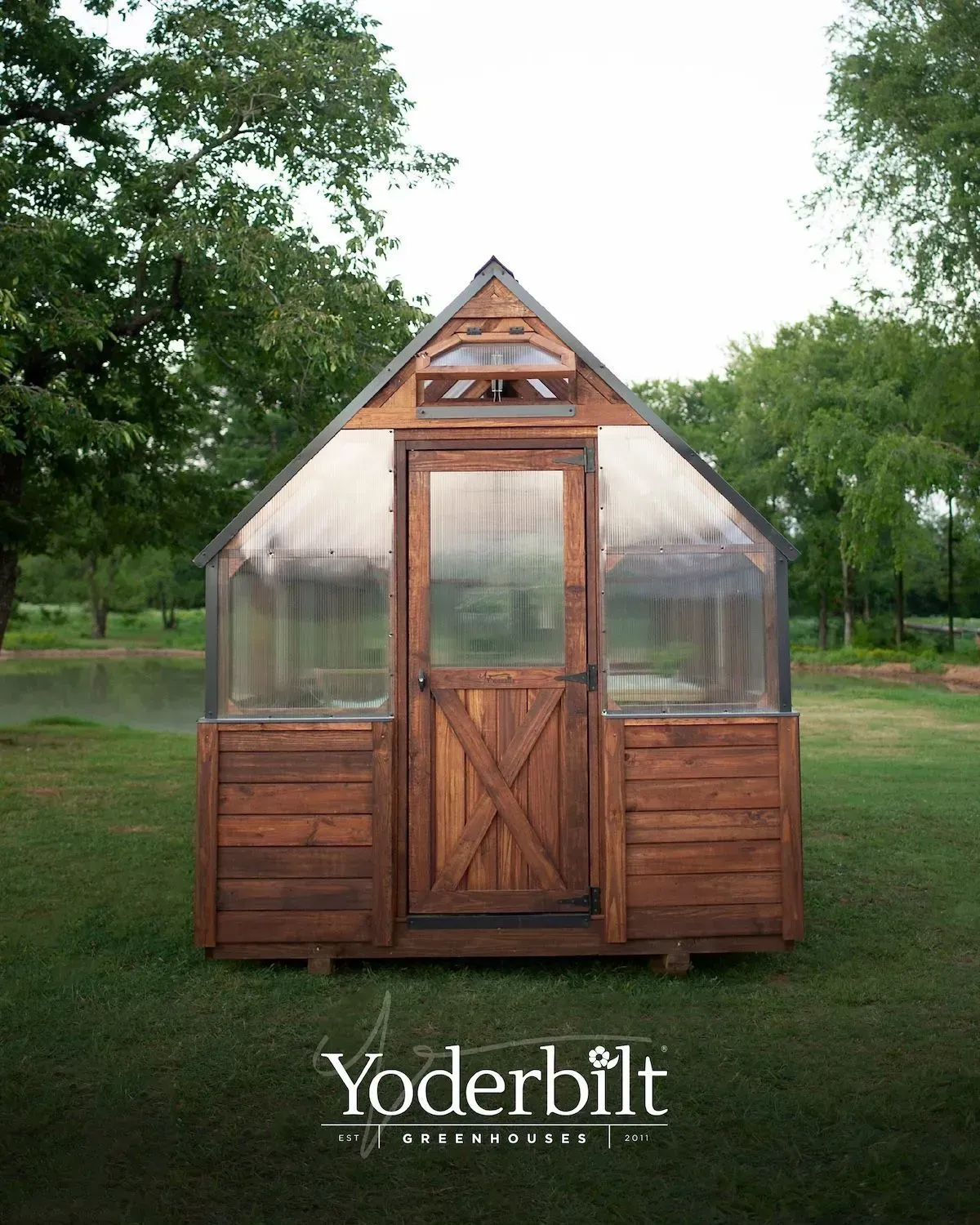 Wooden greenhouse with transparent roof and door, set in a grassy yard.