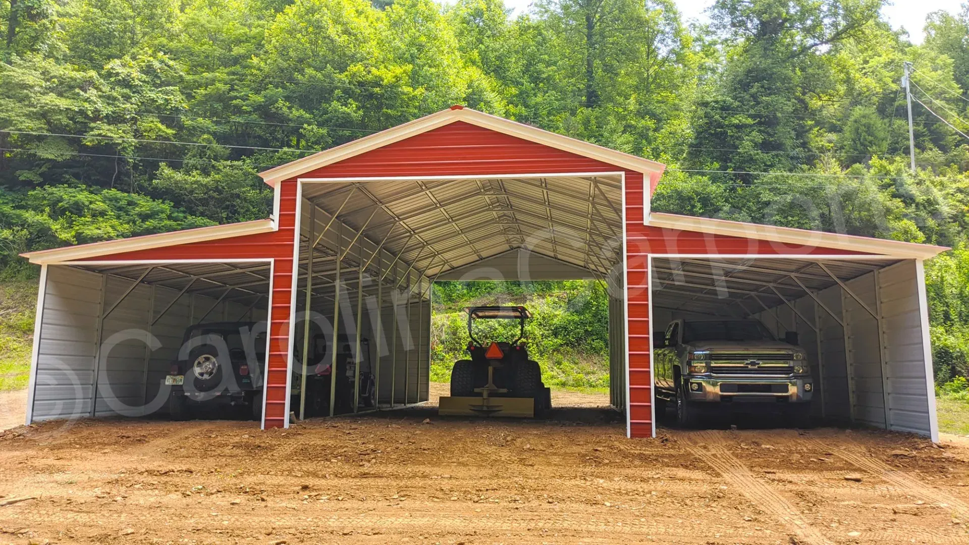 Red and white open-air barn with three bays, housing a tractor, and two vehicles. Set in a wooded area.