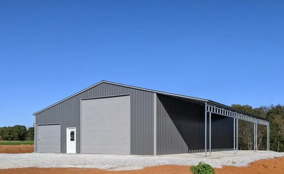 Gray metal barn with open-air lean-to, set against a clear blue sky.