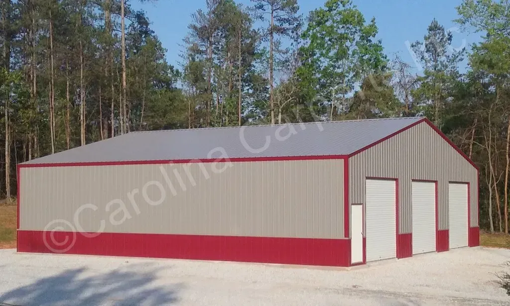 Metal building with gray walls, red trim, and three garage doors, set against a forest.