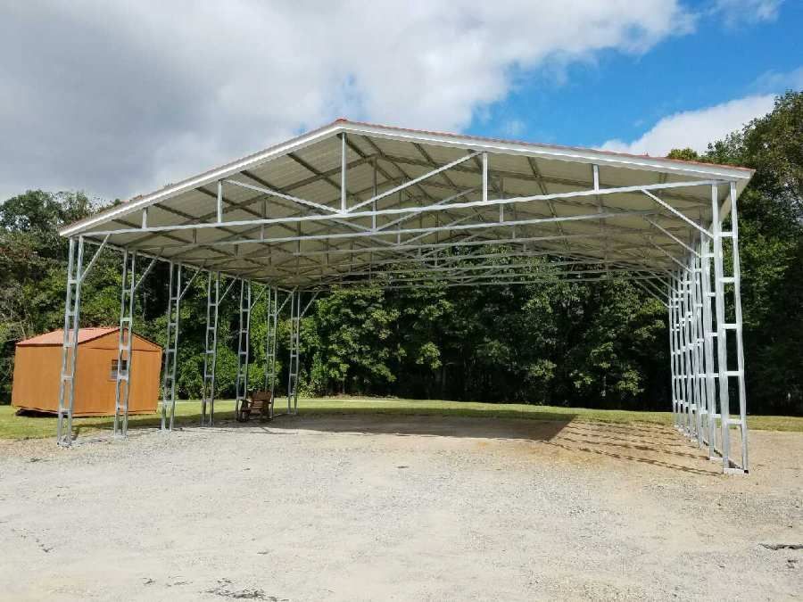 Metal carport structure with gravel ground, tan roof, and small shed in background.