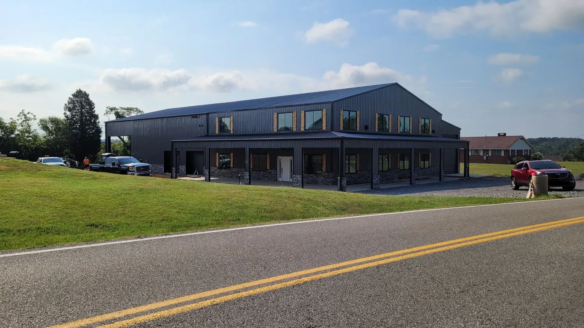 Modern, two-story building with a metal roof and facade, surrounded by a green lawn and a road, under a blue sky.
