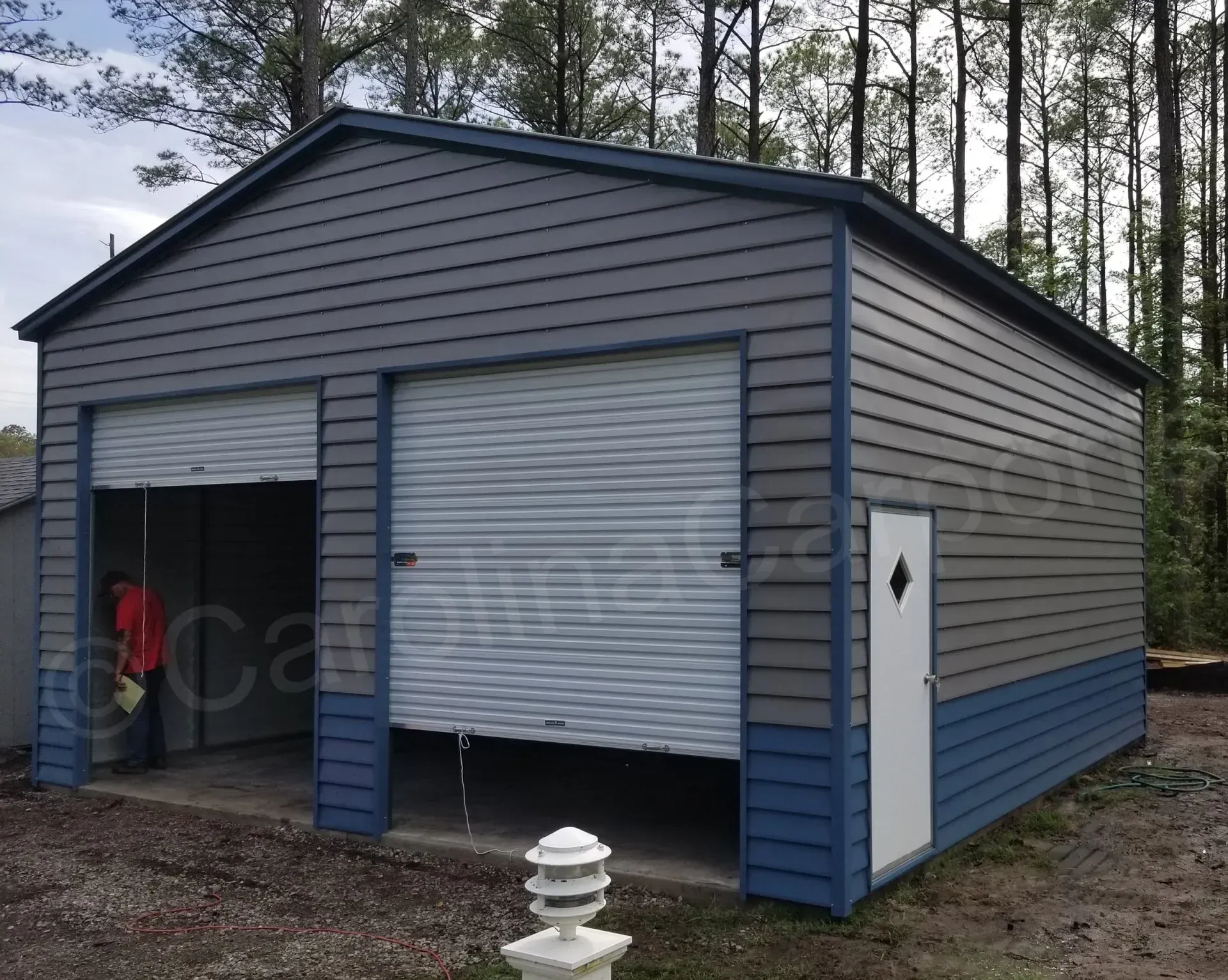 Two-bay metal garage with gray siding, blue trim, two overhead doors, and a side door; outdoors.