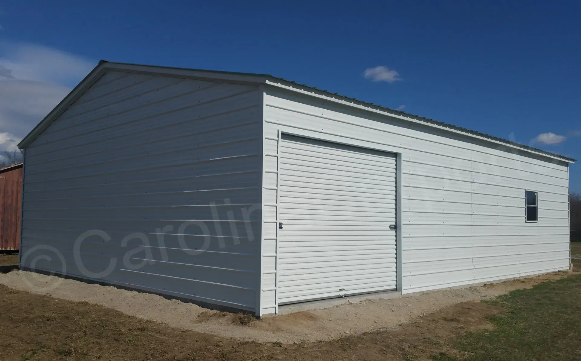 White metal garage with a roll-up door and small window under a blue sky.