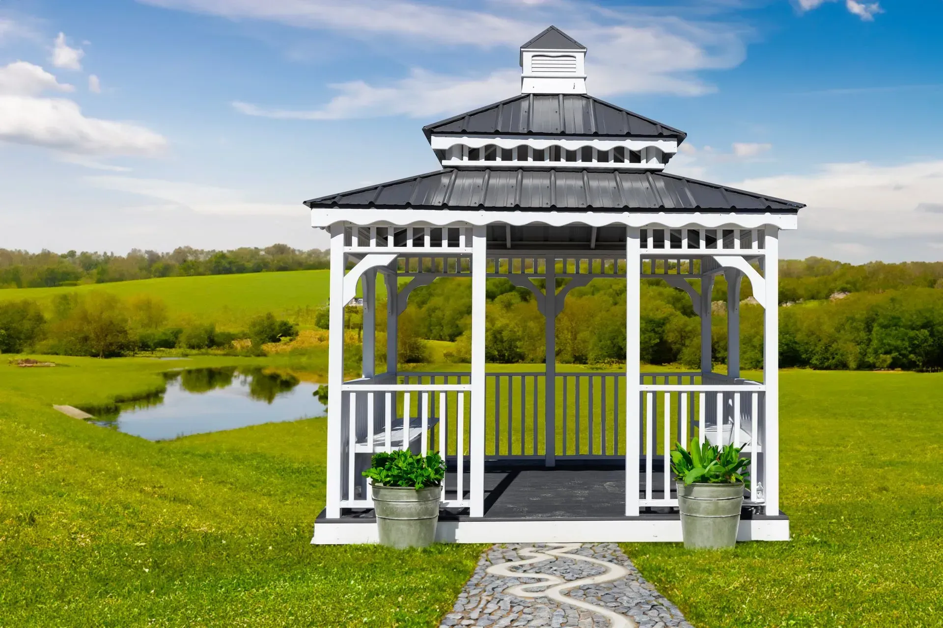 White gazebo with black roof on a green lawn, overlooking a pond.