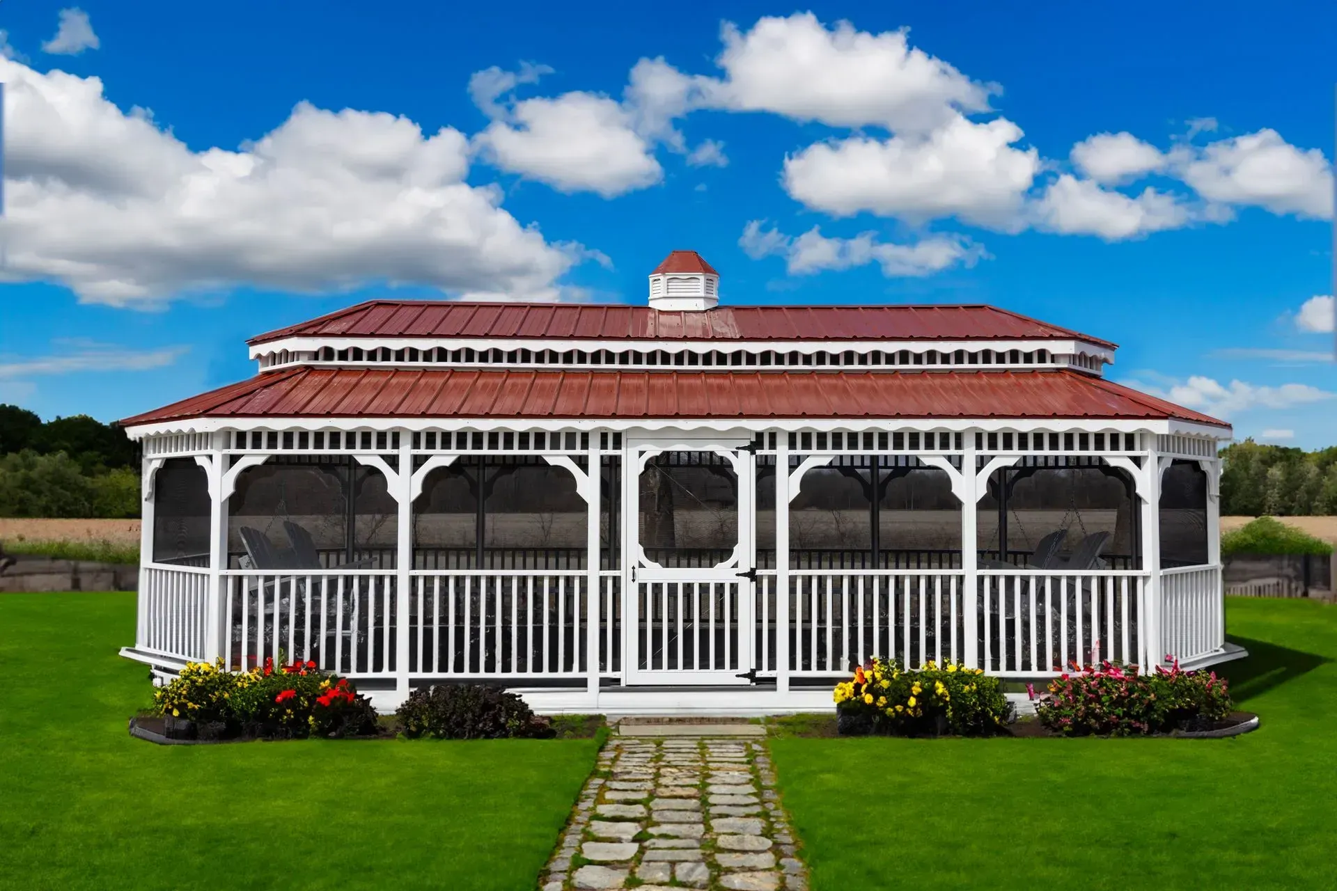 White gazebo with red roof on green grass under blue sky.
