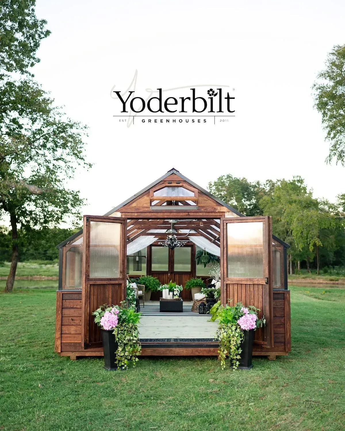 Wooden greenhouse with open doors, decorated with plants, on a green lawn. 