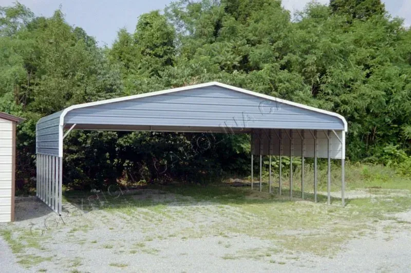 Blue metal carport with open sides, gravel ground, and surrounding green trees.