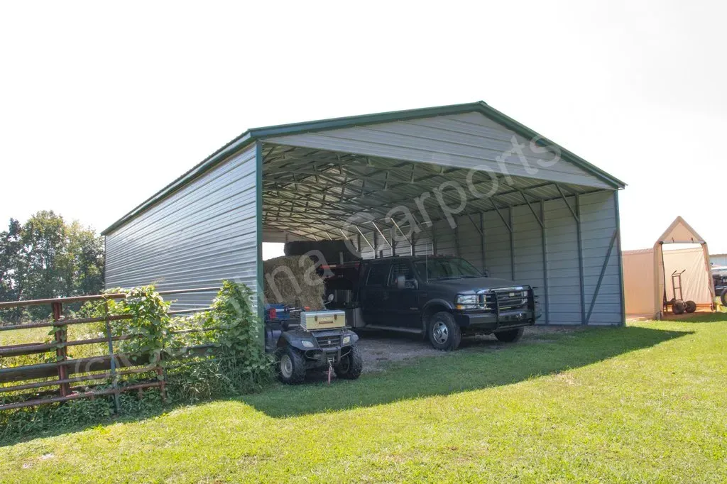 Metal carport with vehicles parked underneath on a grassy field; blue sky in the background.