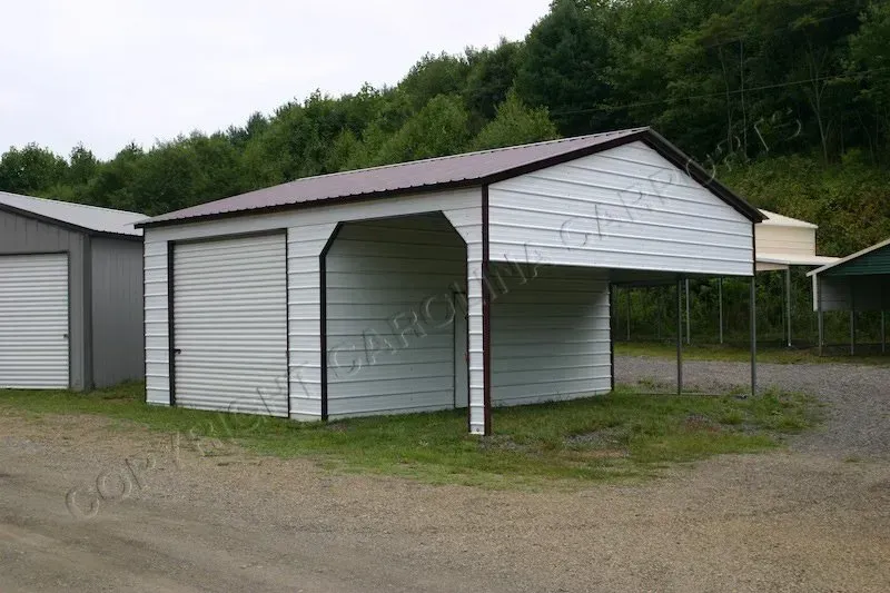 White metal garage with attached carport, brown roof, set on gravel, trees in background.