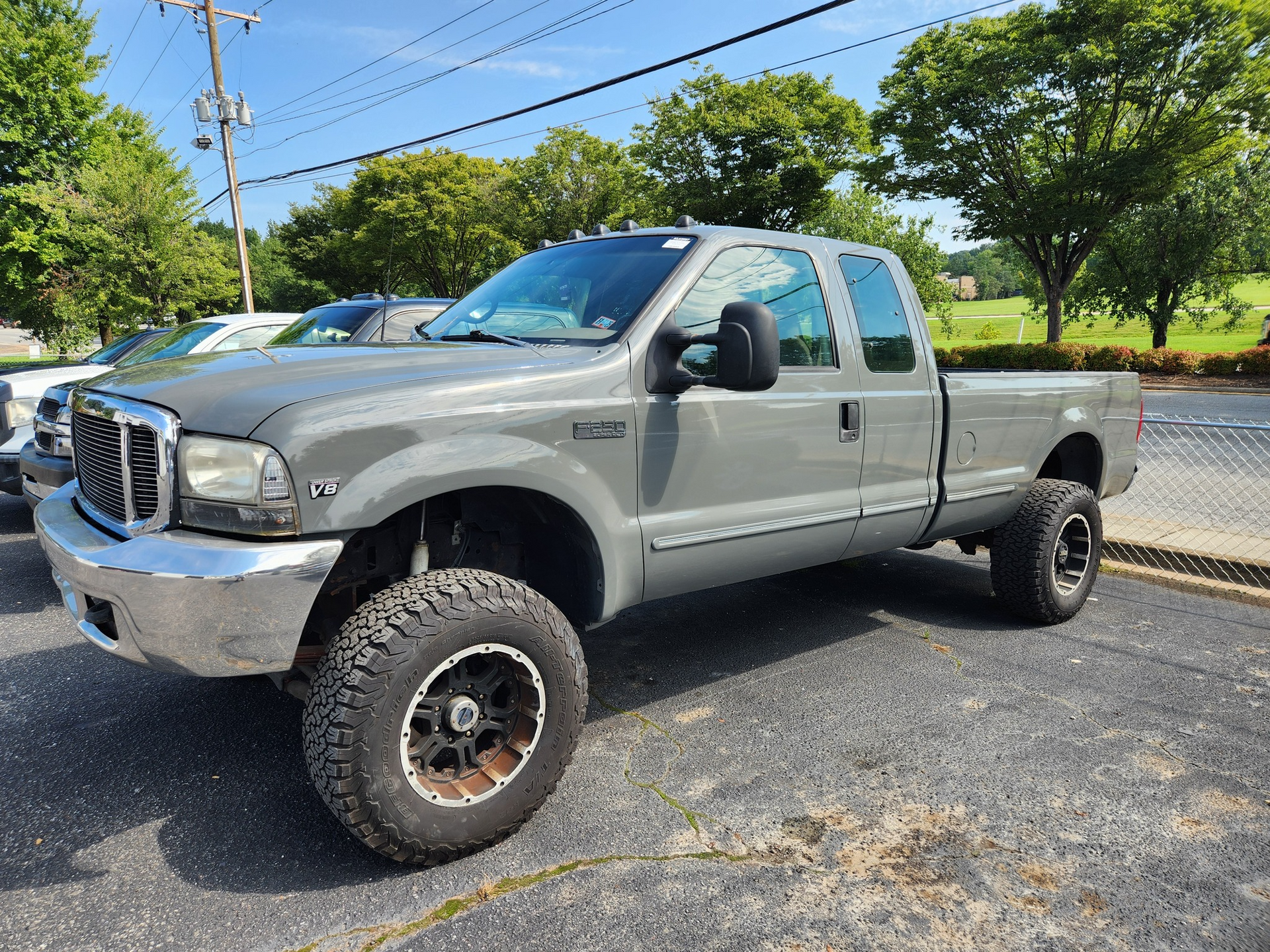 Gray lifted Ford F-250 pickup truck with oversized tires parked on asphalt, sunny day.