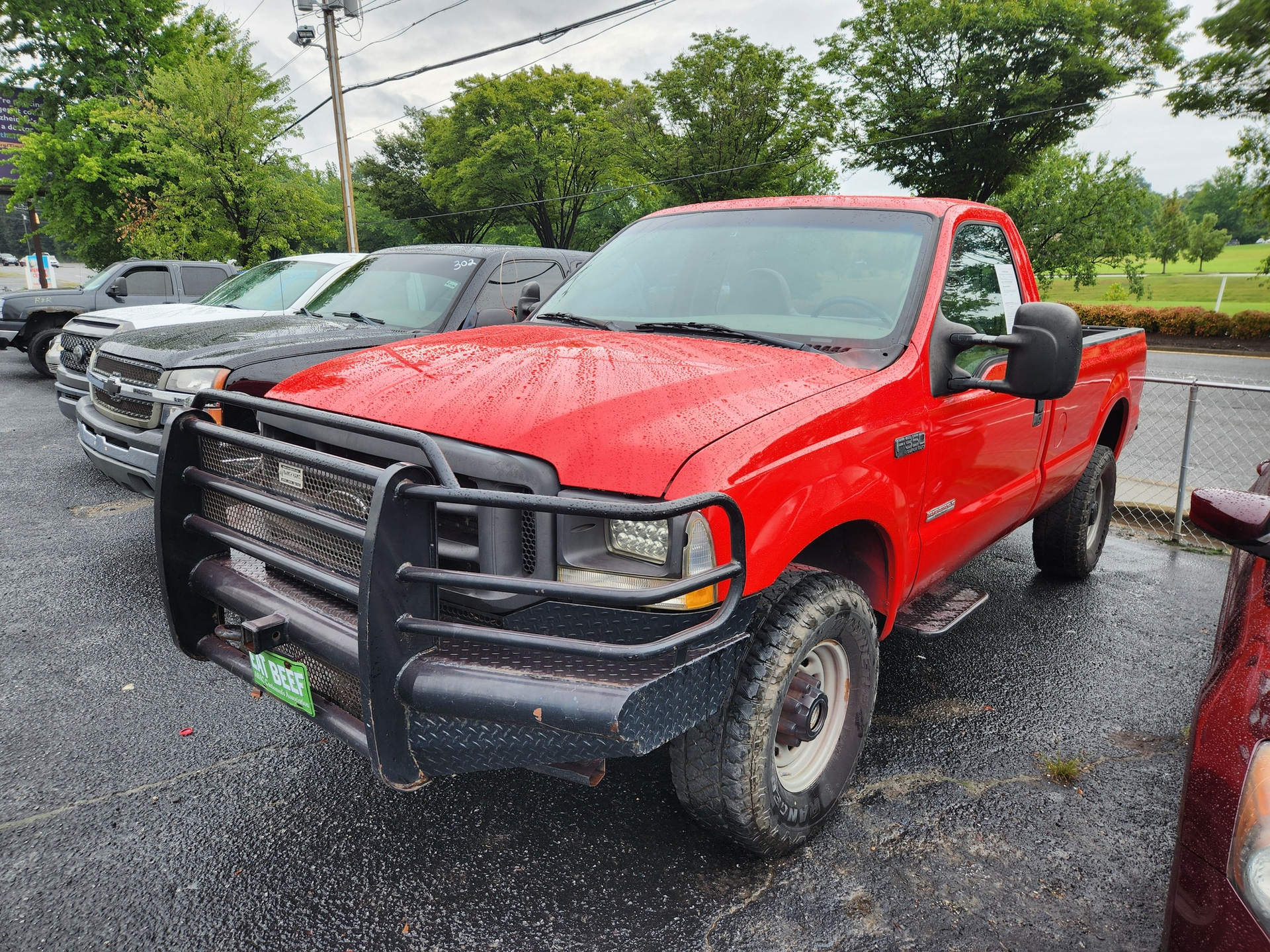 Red Ford pickup truck with a black grill guard parked in a lot with other vehicles.
