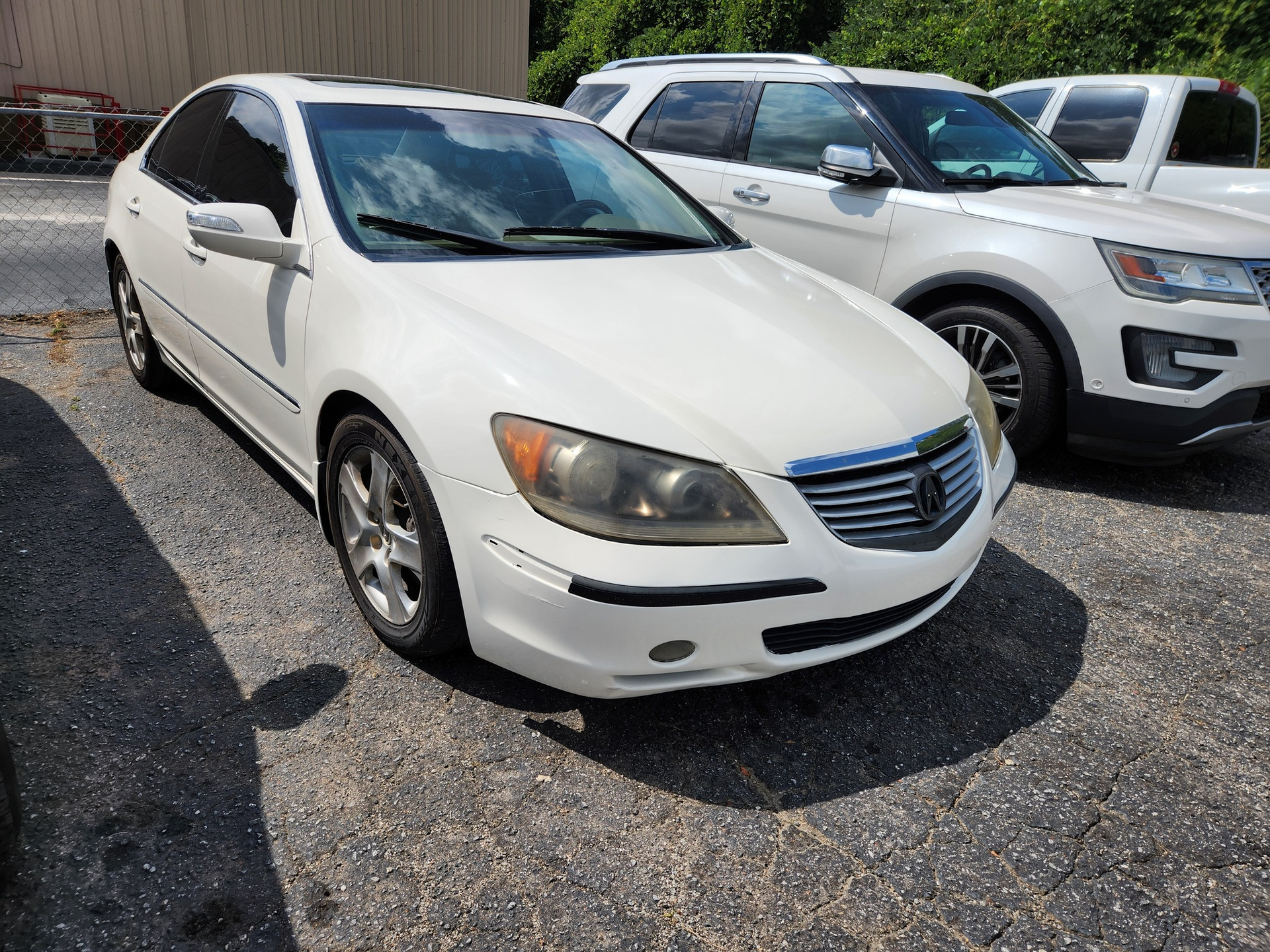 White sedan parked outdoors, next to a white SUV, in a sunny location.