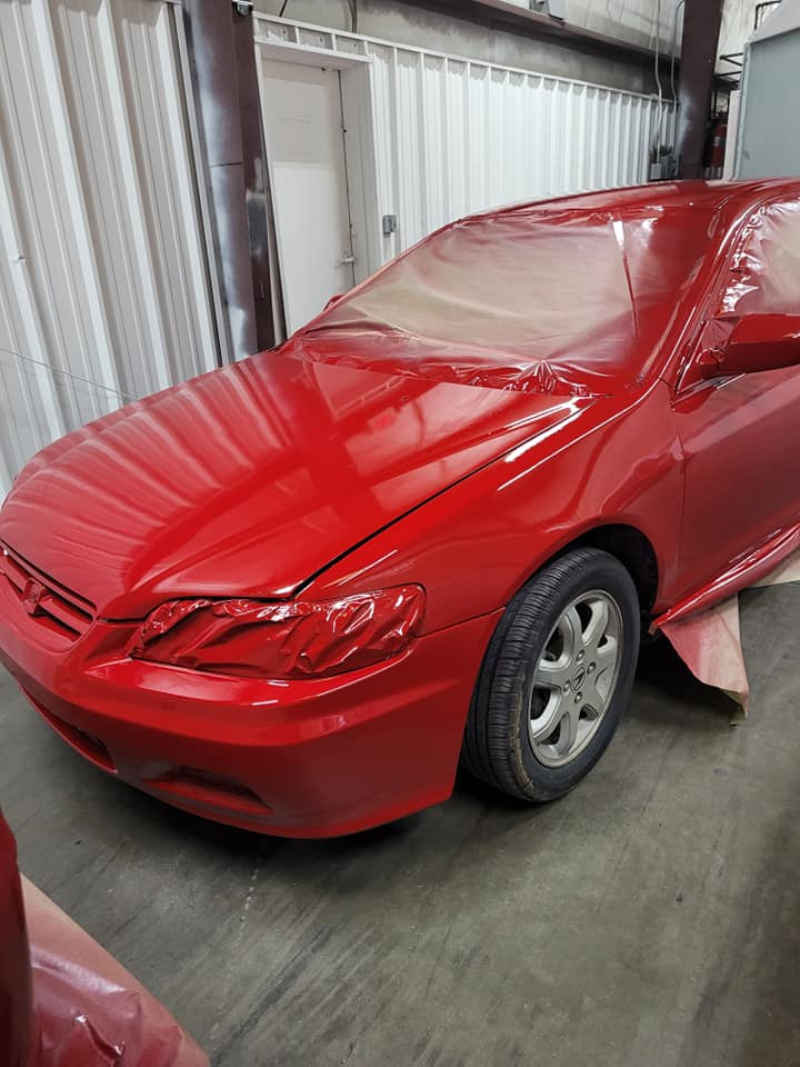 Red car in a body shop, partially painted and covered for protection.