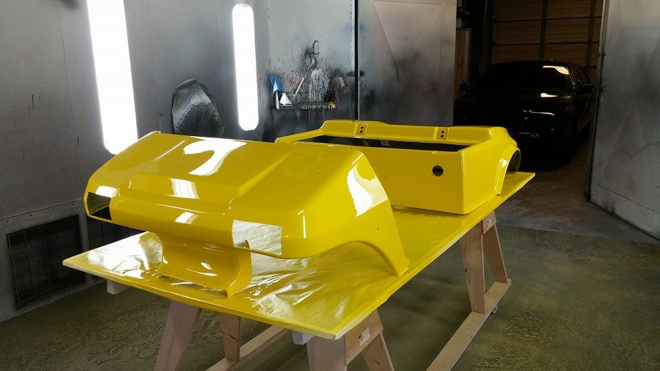 Yellow golf cart body parts freshly painted, drying on a wooden stand in a spray booth.