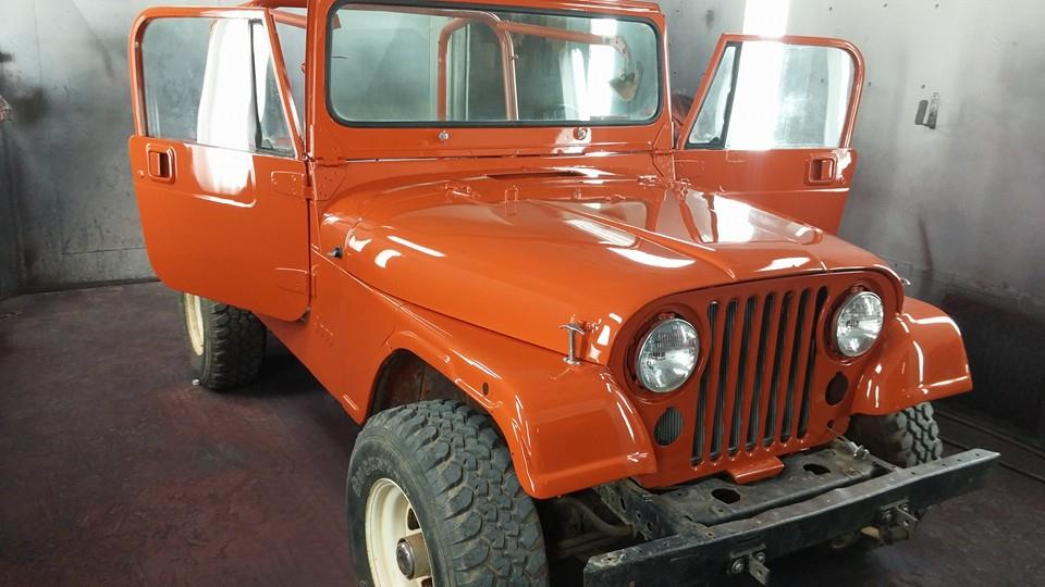 Orange Jeep with doors open, in a workshop. White tires and black front bumper.