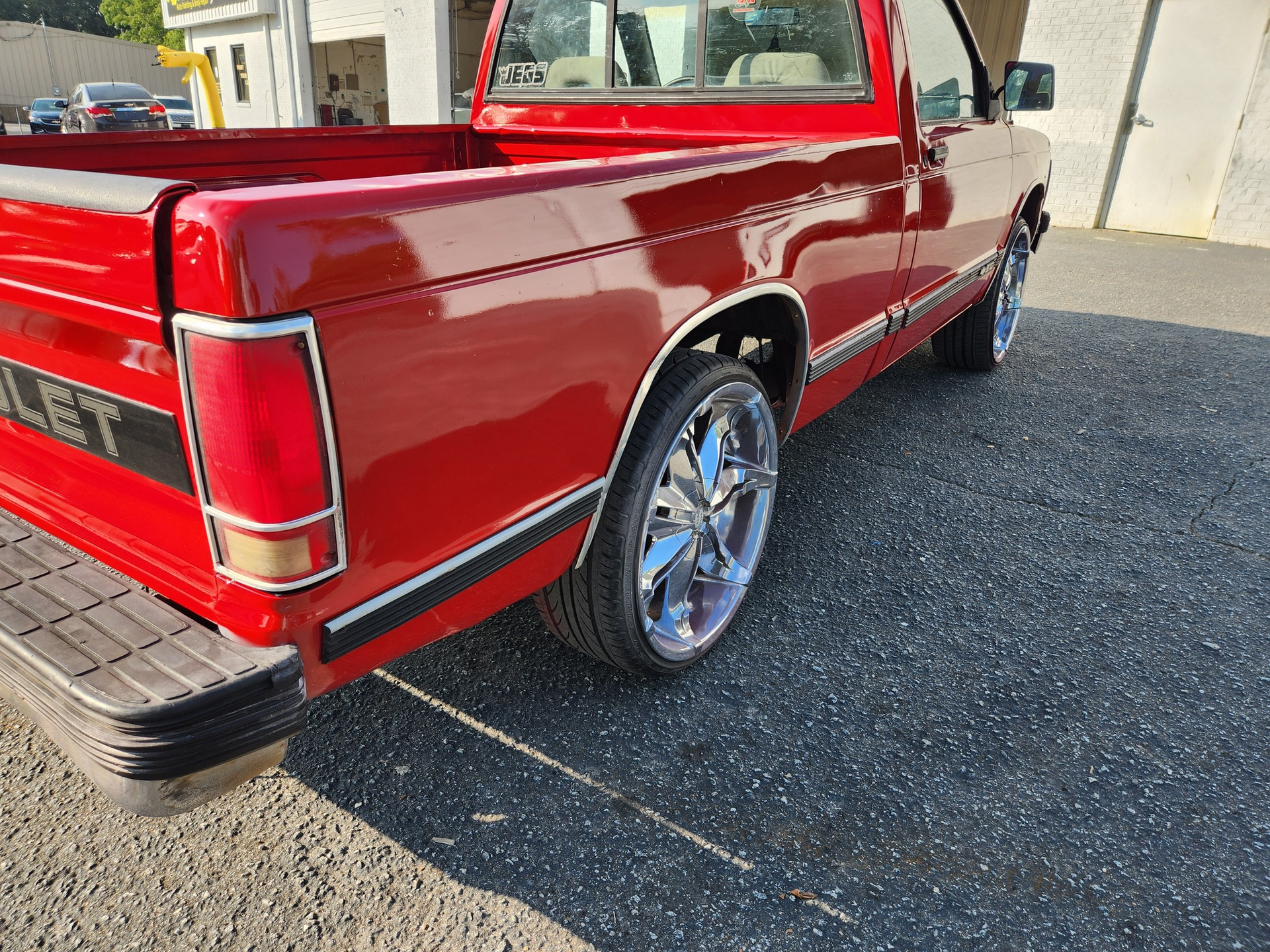 Red Chevrolet pickup truck with chrome wheels parked outside.