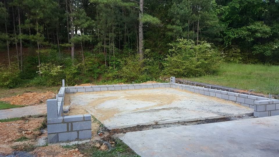 Concrete foundation with a partial cinder block wall perimeter, surrounded by grass and trees in a rural setting.